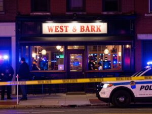 Police investigating a shooting scene outside a bar in West Philadelphia at night.